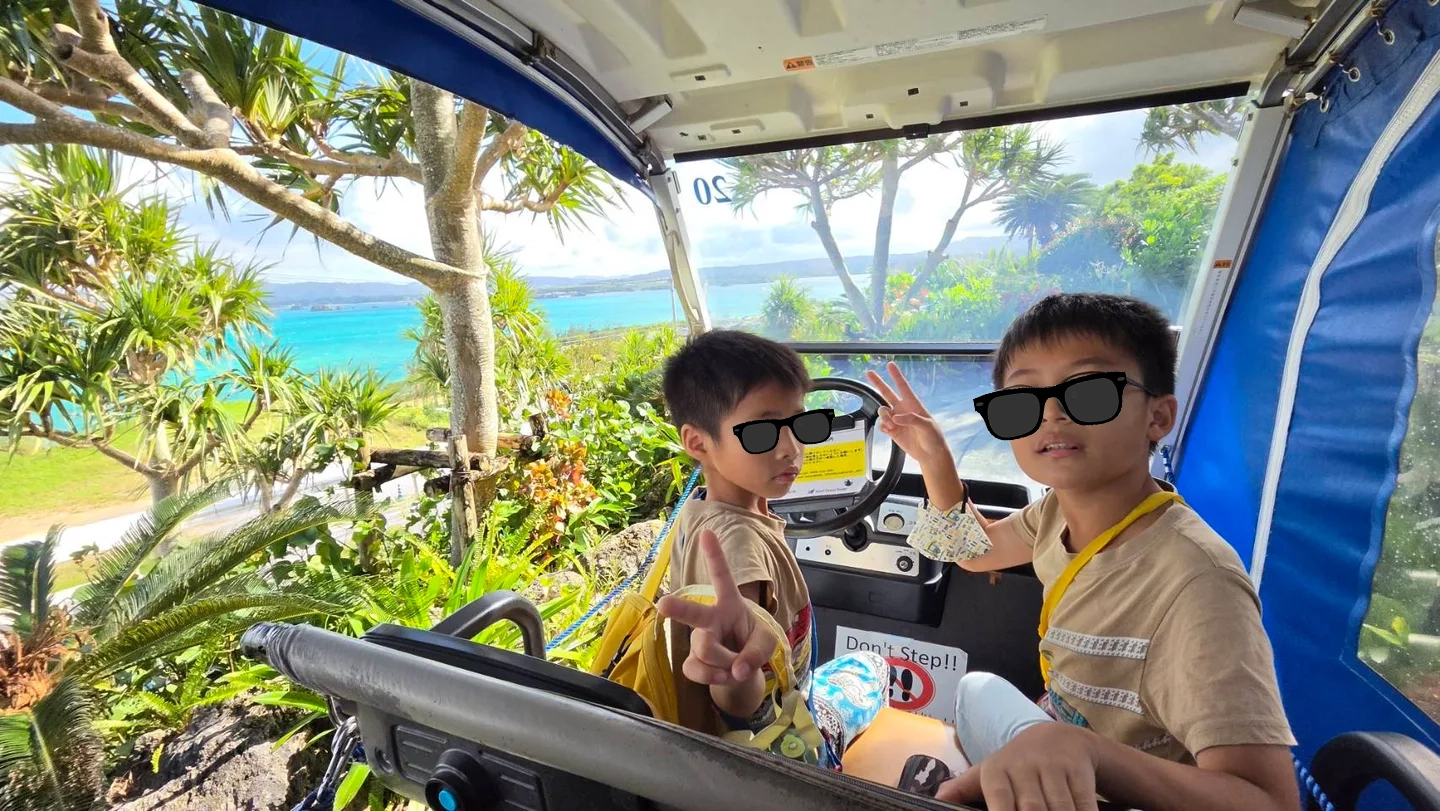 兩個孩子坐在遊園車內,車旁可見海景與綠樹